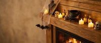 Cozy Halloween fireplace mantel decorated with candles, pumpkins and spooky bat silhouettes creating warm autumn atmosphere for seasonal home decor.