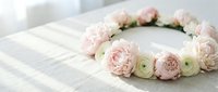 Delicate floral crown with soft pink and white ranunculus flowers arranged in circle on white wooden surface for wedding or special occasion styling.