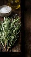 Fresh rosemary sprigs arranged on dark wooden surface with sea salt in ceramic bowl and olive oil bottle, suitable for culinary and cooking content.