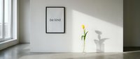 Minimalist interior with a framed be kind quote on a white wall, a yellow tulip in a glass vase, and soft natural light on concrete floor.