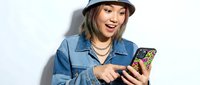 Young woman with long dark hair and fair complexion wearing blue denim shirt and hard hat, smiling while using smartphone for construction or tech industry applications.