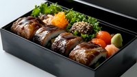 Gourmet sushi rolls with eel sauce in traditional black bento box, garnished with fresh salmon roe, wasabi, and decorative greens, served at Japanese restaurant.