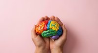 Hands holding colorful rainbow brain model representing mental health awareness, psychology education, neurodiversity and cognitive wellness on pink background.