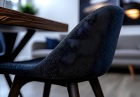 Modern navy blue upholstered dining chair with curved ergonomic backrest shown in close-up detail against blurred contemporary interior background.