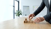 Professional businessman arranging wooden blocks with business icons on office desk representing strategic planning and corporate growth concepts.