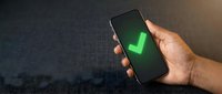 Hand holding smartphone displaying green checkmark on dark screen, symbolizing successful transaction, approval, or verified status for business and technology concepts.