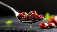 Spoonful of sweet and spicy red chili sauce with dripping oil drop, fresh chilis and herbs on dark background, macro food photography for menu design.