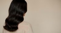 Young Asian woman with long wavy black hair wearing beige sweater against neutral background for beauty and haircare concepts.