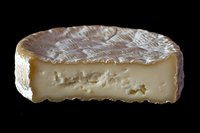 Creamy white Camembert cheese wheel cut in half showing soft interior texture and characteristic white mold rind against dark background. Food photography.