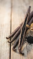Dried vanilla beans with seeds and flower on rustic wooden surface, close-up macro shot for food, cooking, and spice concepts.