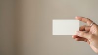 Hand holding blank white business card against neutral beige background, ready for branding mockup, corporate identity design, or professional presentation use.