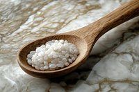 Raw white rice grains in wooden spoon on marble background, close up view of healthy organic cereal in rustic kitchen setting for cooking concept.