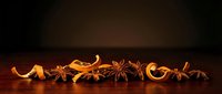 Dried orange slices, star anise, and cinnamon arranged in a row on dark wooden surface with warm lighting for seasonal decoration and culinary styling.