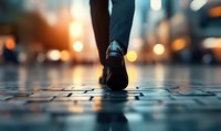 Close-up of business person walking on wet cobblestone street at dusk with bokeh city lights, low angle view showing leather shoe and suit pants leg.