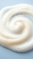 Creamy white cosmetic foam swirl with bubbles on light blue background for skincare and beauty product applications.
