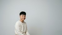 Young man with dark hair and East Asian ethnicity wearing a cream-colored long-sleeve shirt, smiling at camera against neutral background. Suitable for portrait, lifestyle, and business applications.