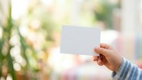 Hand holding blank white card with blurred garden background, suitable for business cards, invitations, promotional materials, and marketing presentations.