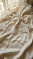 Luxurious cream silk fabric with ornate lace trim featuring intricate floral embroidery and scalloped edges, draped elegantly for wedding, bridal, or formal event design projects.