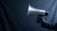 Hand holding white megaphone against dark dramatic background for communication and announcement concepts in business presentations.
