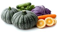 Fresh seasonal vegetables and fruits on white background. Gray pumpkins, purple cabbage, orange carrots, cucumber and citrus slices arranged in composition.