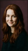 Young Caucasian woman with long auburn hair smiling warmly in professional portrait against burgundy background for business headshots and corporate use.