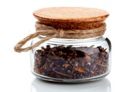 Glass jar with dried cloves and wooden cork lid on white background, spice storage concept for cooking and aromatherapy uses.