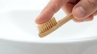 Hand holding natural bamboo toothbrush over white bathroom sink for eco-friendly oral hygiene and sustainable dental care routine.