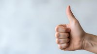 Hand showing thumbs up gesture against neutral background expressing approval, success, and positive feedback for business presentations.