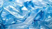 Crumpled blue plastic bag texture with folds and wrinkles creating abstract pattern. Translucent material catching light for environmental concept or packaging design.