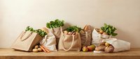 Eco-friendly reusable shopping bags filled with fresh organic vegetables and groceries on wooden table promoting sustainable zero waste lifestyle.