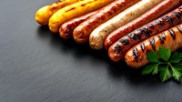 Grilled assorted sausages with char marks arranged in row on dark slate background with fresh parsley garnish. For menu, food photography and cooking blogs.