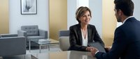 Professional businesswoman in gray suit meeting with male colleague in modern office setting for corporate consultation and partnership discussions.