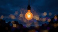Glowing vintage light bulb suspended against blurred night cityscape with bokeh lights, symbolizing innovation, ideas, and creative solutions for business and design projects.