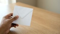 Hand holding white envelope on wooden desk surface, suitable for business correspondence, mail delivery, and communication concepts.