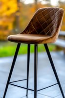 Modern brown leather bar stool with quilted pattern seat and black metal legs against blurred autumn background, contemporary furniture design.