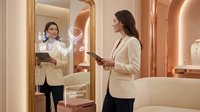 Professional businesswoman in white blazer checking tablet device in modern luxury hotel bathroom with golden mirror and warm ambient lighting.