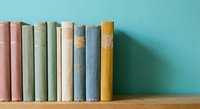 Row of vintage books with colorful spines arranged on wooden shelf against turquoise wall for home decor and reading inspiration.