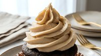 Chocolate cupcake topped with swirled caramel frosting, served on white plate with gold fork and napkin for dessert, bakery, and food styling.