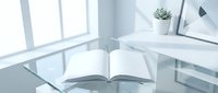 Open book on glass desk in bright modern office workspace with laptop and succulent plant creating minimalist productive environment for reading and work.