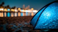 Glowing blue camping tent on sandy beach at night with blurred city lights and water reflections creating magical outdoor atmosphere. Perfect for adventure concepts.