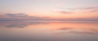 Serene sunset over calm water with soft pink and purple hues reflecting on glassy surface, ideal for peaceful backgrounds and nature-inspired design projects.