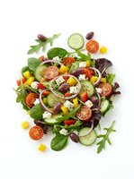 Fresh garden salad with mixed greens, tomatoes, cucumbers, olives, and feta cheese arranged on white background for healthy eating and nutrition content.