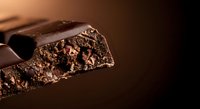 Dark chocolate bar with nuts broken to show textured interior with cocoa nibs and roasted pieces on black background for gourmet food photography.