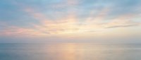 Serene ocean horizon at sunrise with soft pastel pink, blue, and golden light reflecting on calm water surface, peaceful seascape for relaxation and wellness projects.