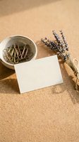 Blank white card with dried lavender flowers and paper clips in ceramic bowl on textured beige surface for branding and stationery design mockup.