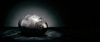 Ornate silver egg with intricate engravings resting on dark textured surface against moody black background for luxury product photography and elegant design projects.
