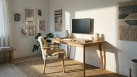 Bright home office workspace with wooden desk, comfortable chair, and monitor, featuring gallery wall art and natural sunlight for productive work environment.