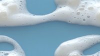 Foamy white soap bubbles floating on bright blue water surface creating abstract cleansing and hygiene concept for bathroom and spa wellness applications.