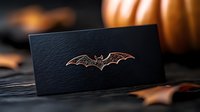 Copper metallic bat design on black textured card against dark moody background with autumn decorative elements and pumpkin silhouette for Halloween season.