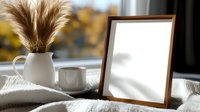 Cozy autumn morning setup with blank wooden frame, white ceramic vase with pampas grass, coffee cup and soft blanket near window with natural light and bokeh.
